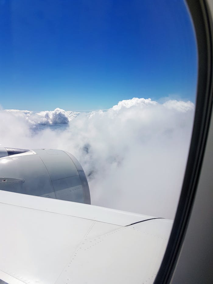 A serene view of an airplane wing with clouds and blue sky from a window seat.